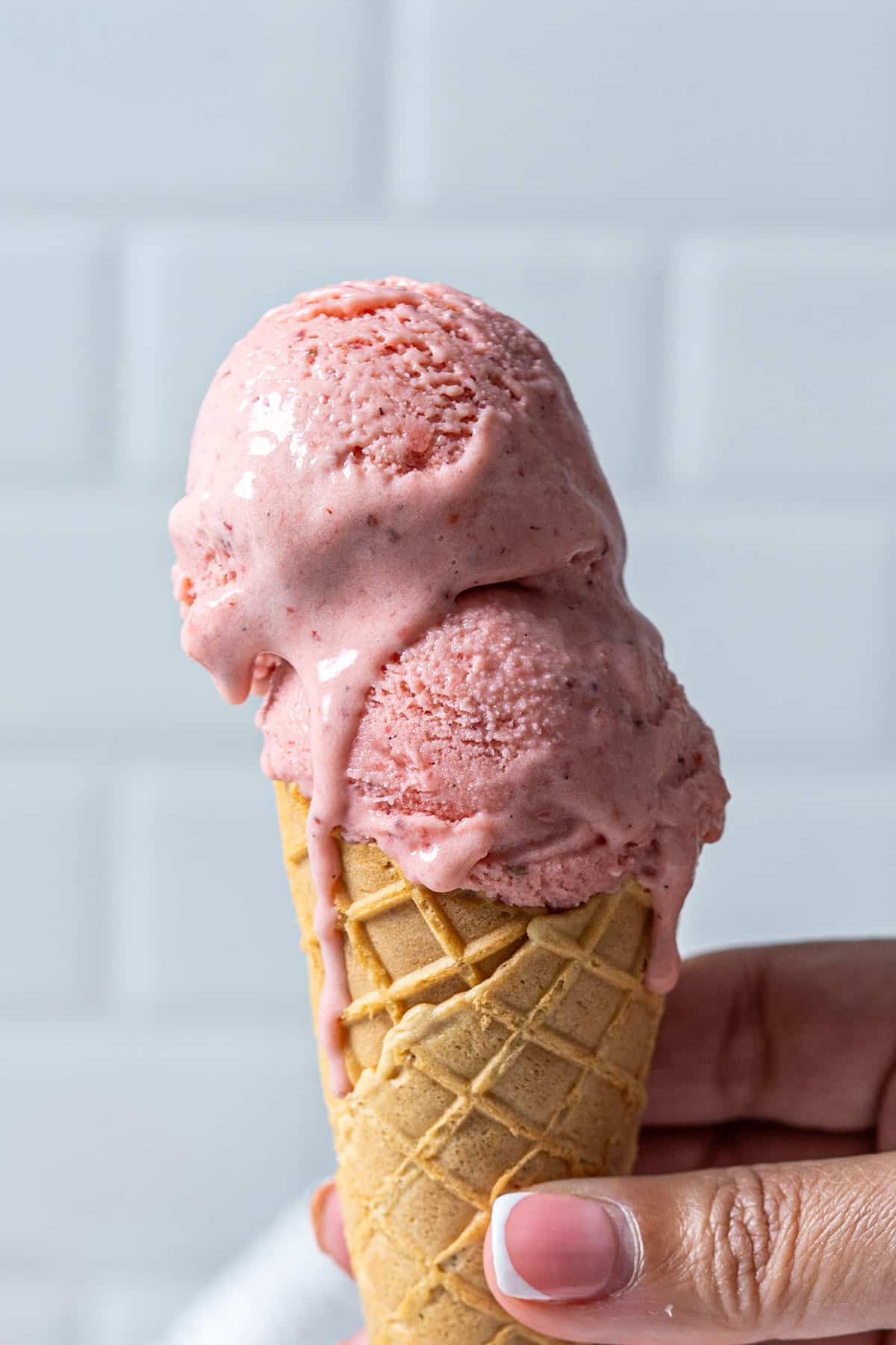 Holding strawberry ice cream in an ice cream cone.